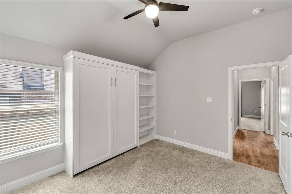 Built-in cabinetry with integrated shelving, vaulted ceiling, ceiling fan, and window with blinds