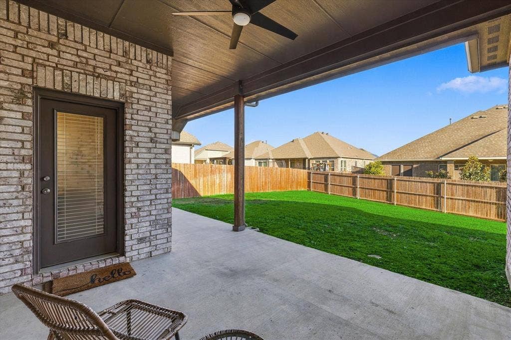 Covered patio with a ceiling fan, concrete flooring, brick exterior, and a wood privacy fence enclosing a grass lawn