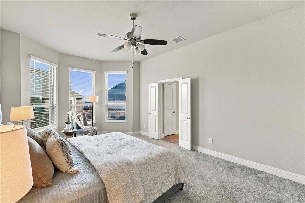 Bay window with three windows, gray carpet flooring, ceiling fan with light fixture, and white bi-fold doors