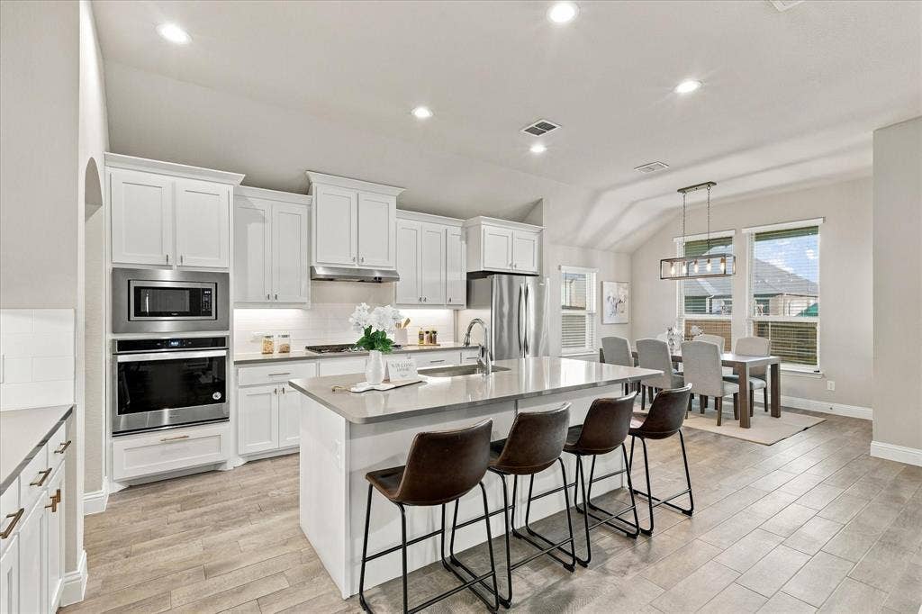 Modern kitchen featuring white cabinetry, stainless steel appliances, a large center island, wood-finish flooring, and recessed lighting