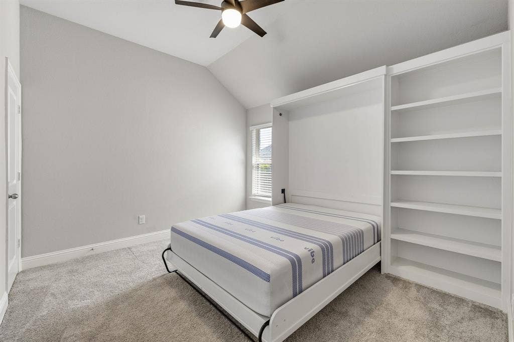 Room with vaulted ceiling, plush carpeting, built-in shelving, and a wall-mounted bed system