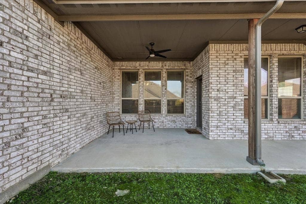 Covered patio featuring a ceiling fan, light gray brick exterior, and multiple windows