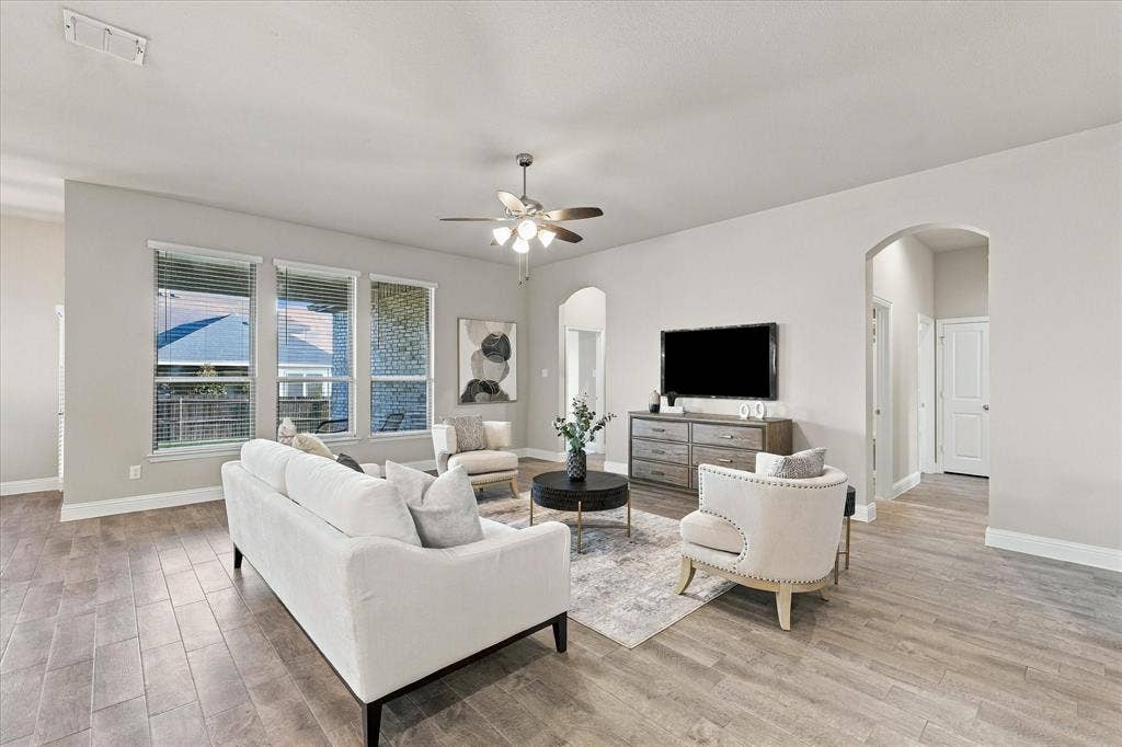 Spacious living area featuring wood-finish flooring, a ceiling fan, and multiple windows with blinds