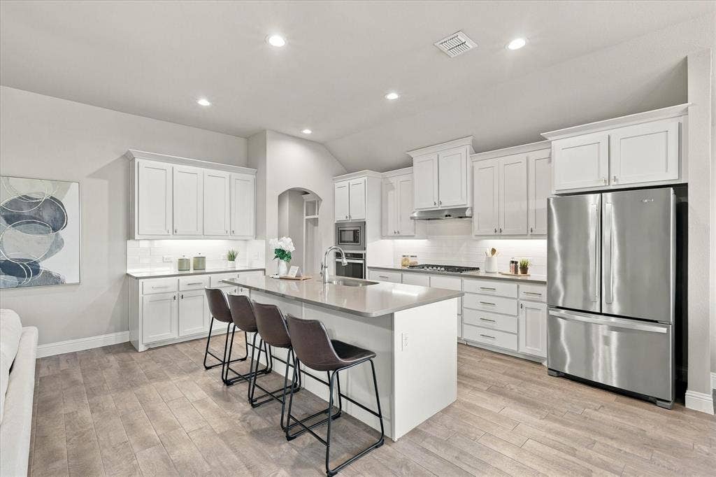 Spacious kitchen with a central island, white cabinetry, integrated stainless-steel appliances, recessed lighting, and wood-finish flooring