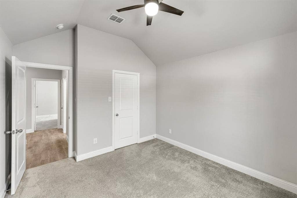 Vaulted ceiling with an attached ceiling fan, light gray wall paint, and gray carpet flooring