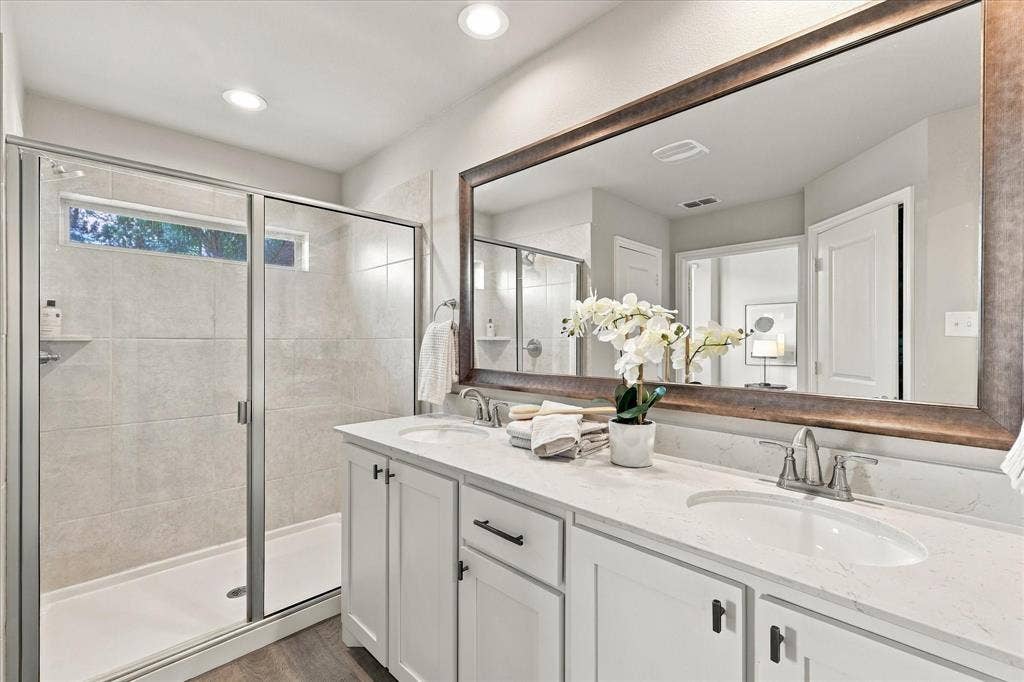Dual vanity with white cabinetry and integrated sinks, a large framed mirror, and a glass-enclosed shower with tiled walls
