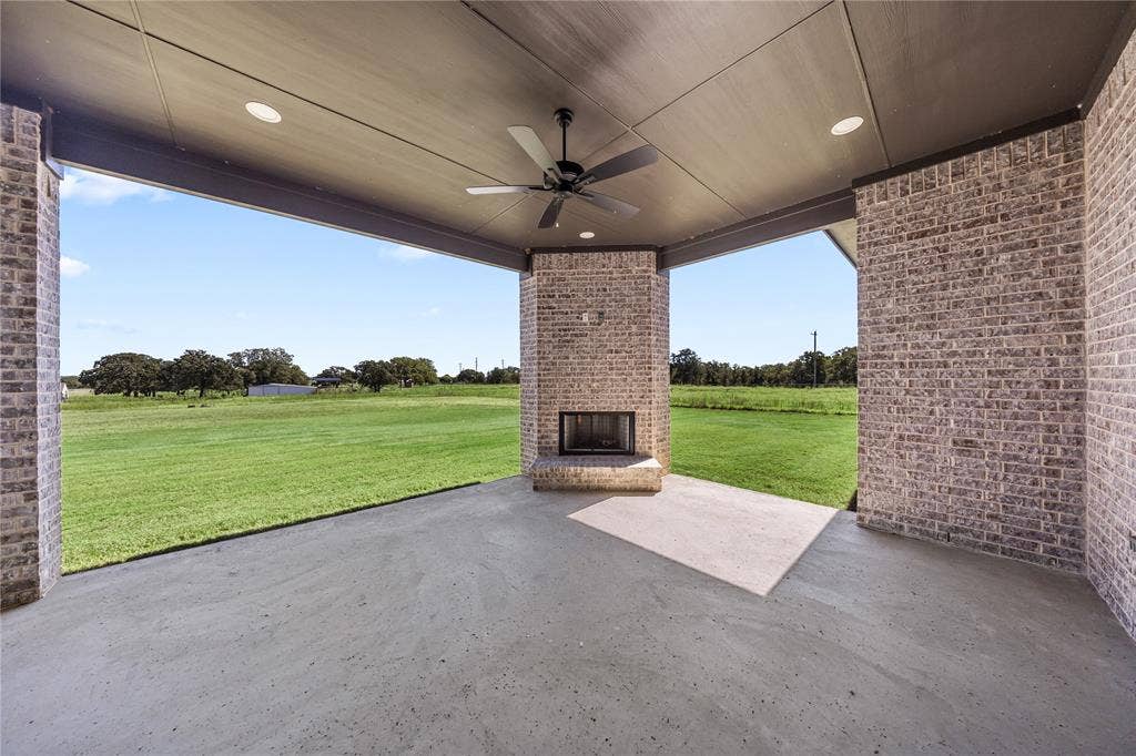 Covered patio featuring a brick fireplace, concrete flooring, recessed lighting, and a ceiling fan