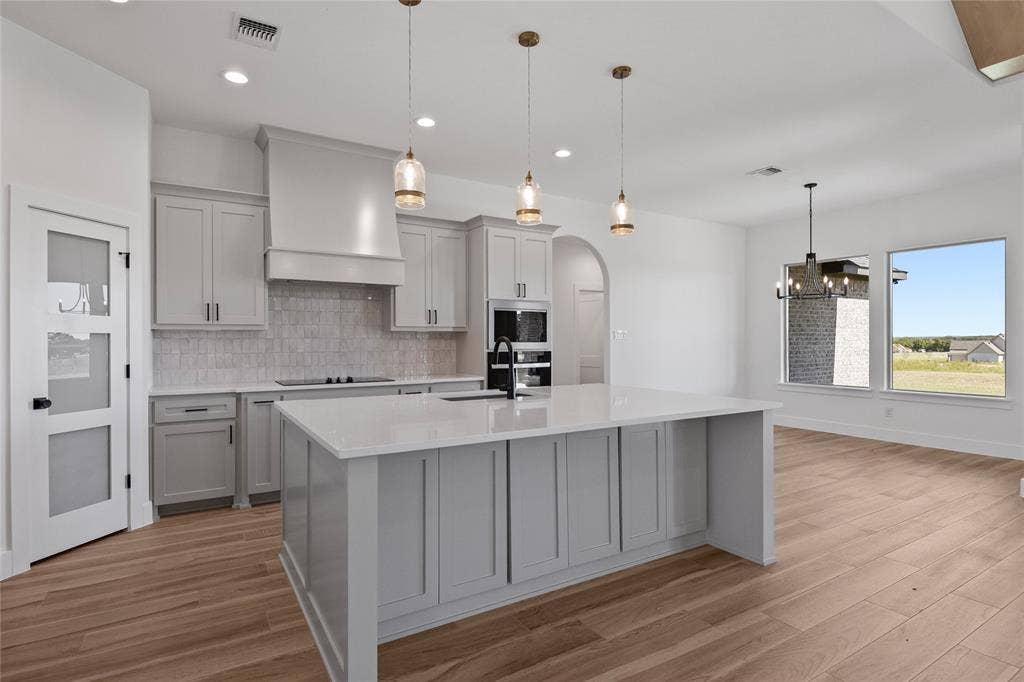 Kitchen featuring a large island with white countertop, light gray cabinetry, built-in appliances, and wood-finish flooring