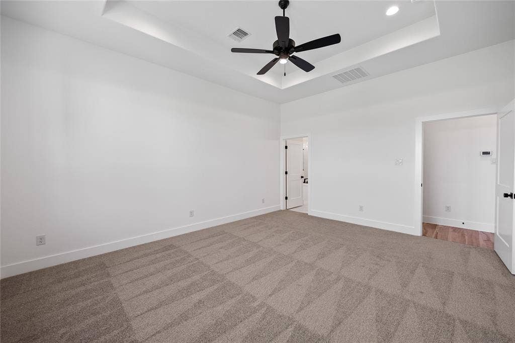 Spacious room featuring tray ceiling with recessed lighting, ceiling fan, neutral carpeting, and white walls