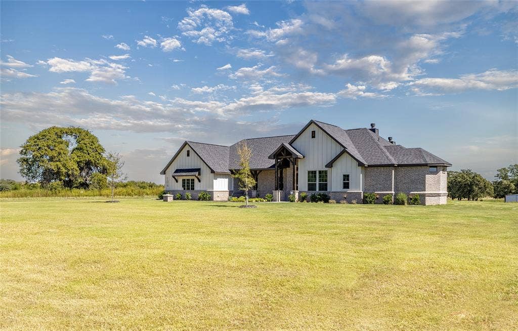 Ranch-style residence featuring a combination of brick and vertical siding, a dark shingled roof, a covered entryway with exposed wood beams, and a landscaped foundation