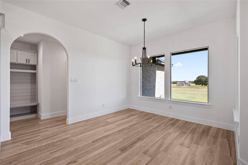 Wood-finish flooring, recessed built-in shelving with cabinetry, arched entryway, and modern chandelier