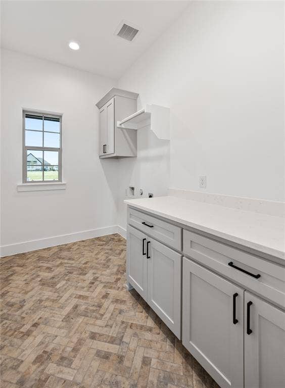 Herringbone pattern flooring, light gray cabinetry with black hardware, white countertops, and a window providing natural illumination