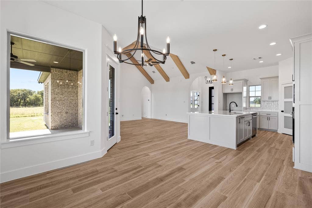 Open concept living space featuring wood-finish flooring, vaulted ceilings with exposed beams, and a kitchen island with a built-in sink