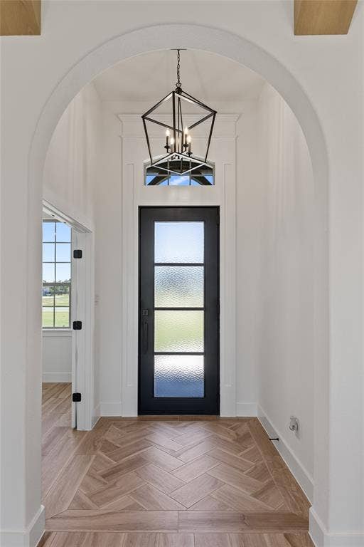 Arched entryway with a black multi-paneled door, transom window, and an overhead geometric chandelier