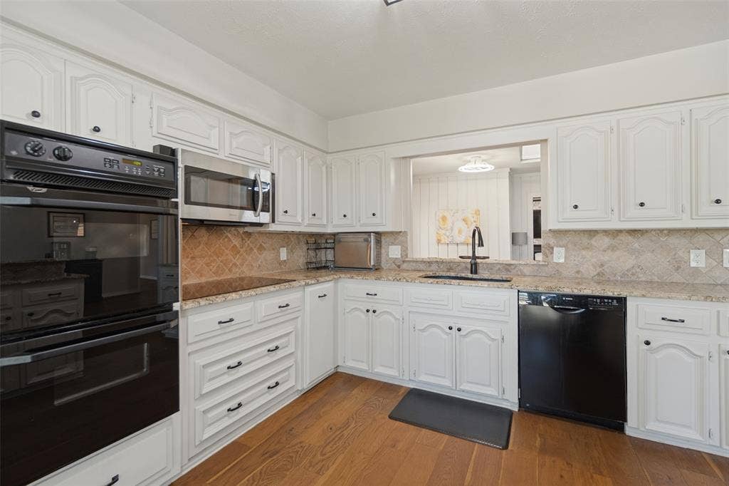 7414 Windmill Lane, Garland, TX 75044 Kitchen featuring white cabinetry, granite countertops, a tiled backsplash, and wood-finish flooring