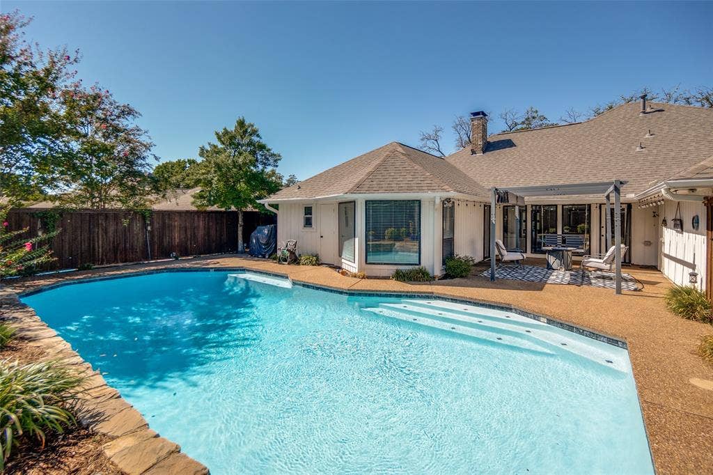 7414 Windmill Lane, Garland, TX 75044 Expansive backyard featuring a clear water swimming pool, stone coping, and a textured concrete patio
