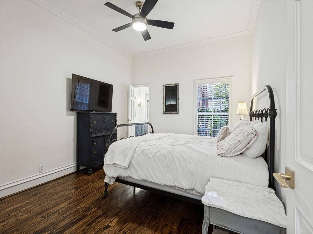 Hardwood flooring with a rich finish, crown molding, white window shutters, and a ceiling fan with integrated lighting
