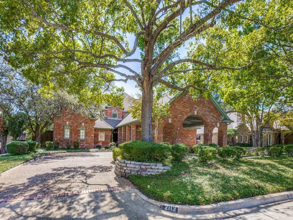 Brick exterior with gabled roofline, mature tree, stone-stacked landscaping, and arched drive-through portico