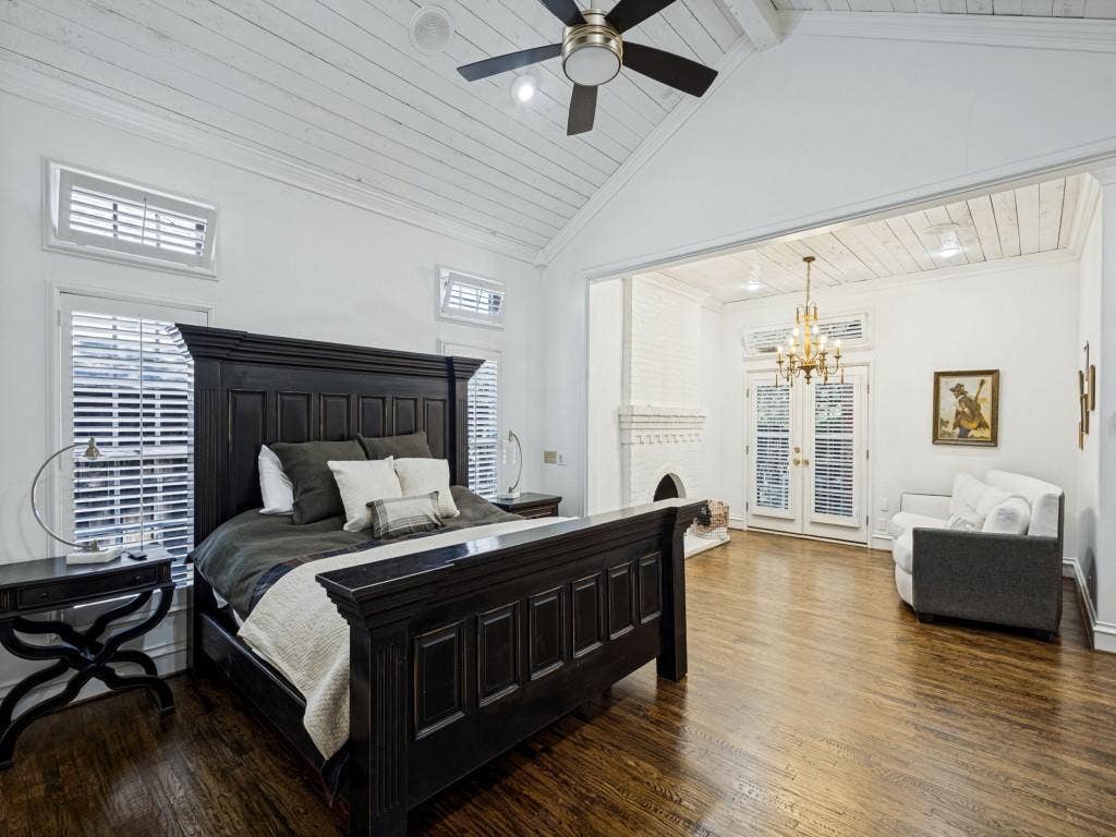 Vaulted ceiling with wood-finish planks, wood-finish flooring, plantation shutters, French doors, and a decorative fireplace