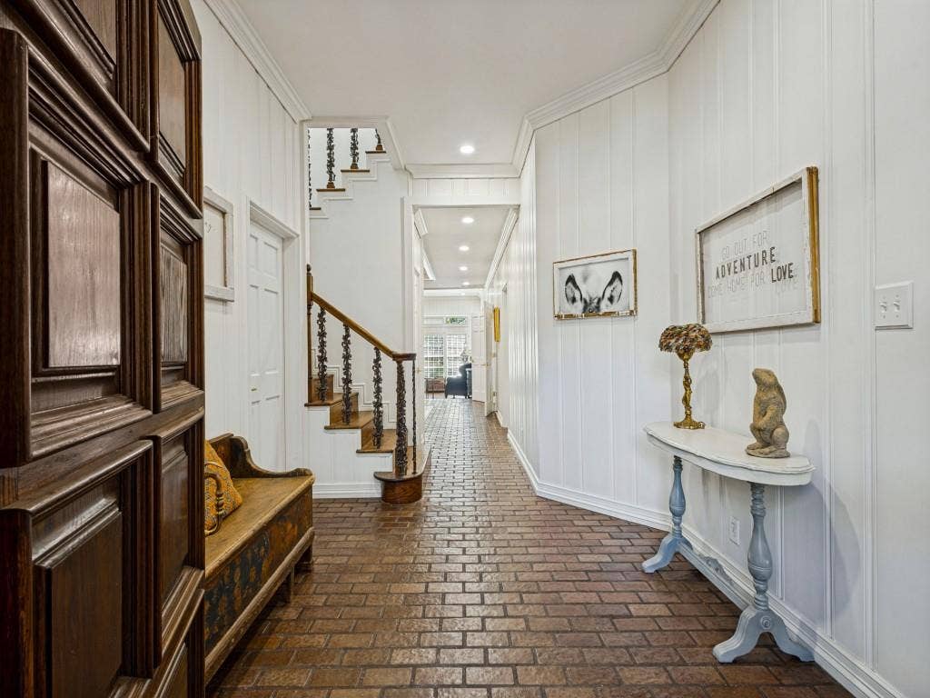 Brick flooring, white vertical paneled walls, crown molding, wood staircase with iron balusters, and recessed lighting