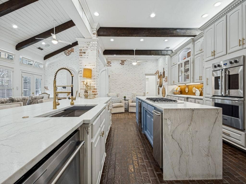 Vaulted ceiling with exposed beams, brick accent walls, and wood-finish flooring