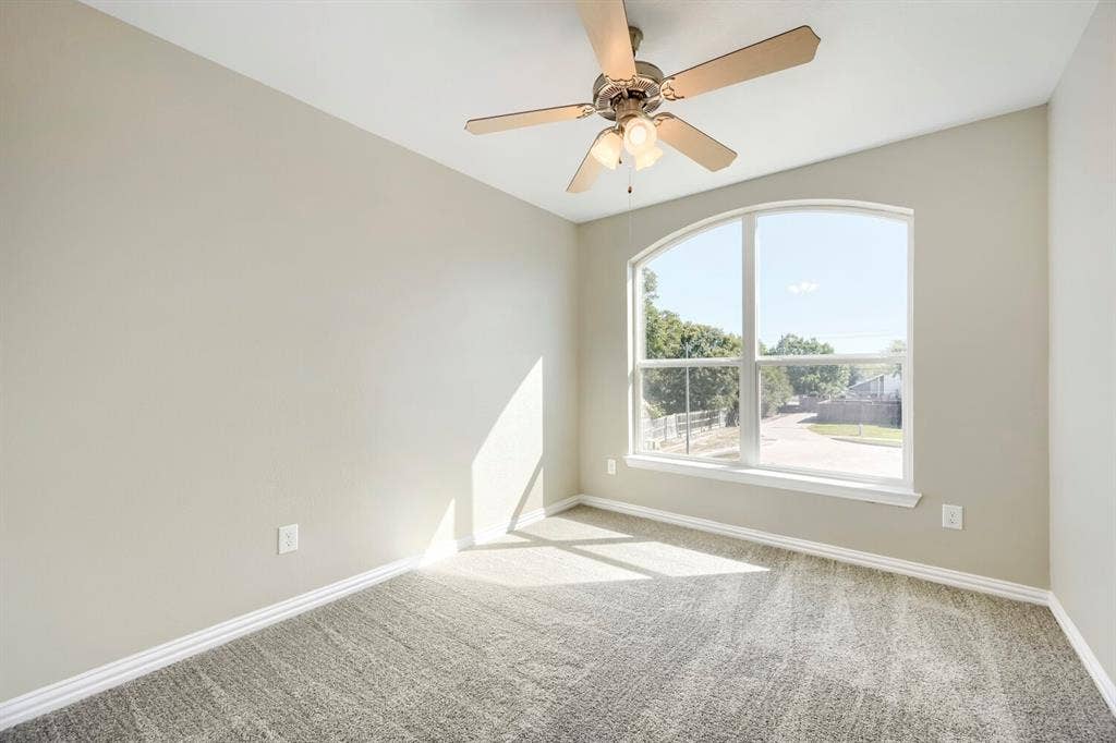 Vaulted ceiling with a ceiling fan, arched window, and textured carpet flooring