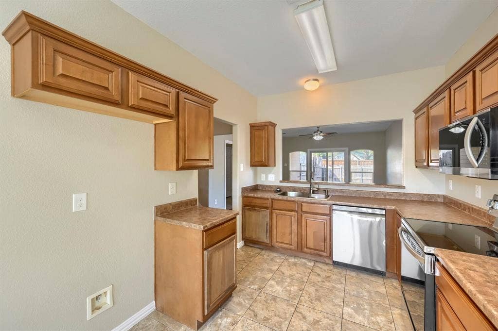 Kitchen featuring wood cabinetry, laminate countertops, a stainless steel dishwasher, a built-in microwave, and tile flooring