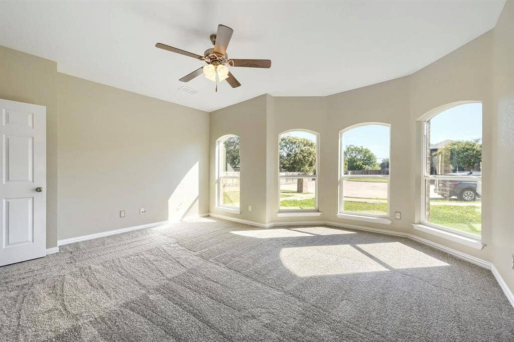 Recessed ceiling with a ceiling fan, arched windows, light-toned walls, and grey carpeting