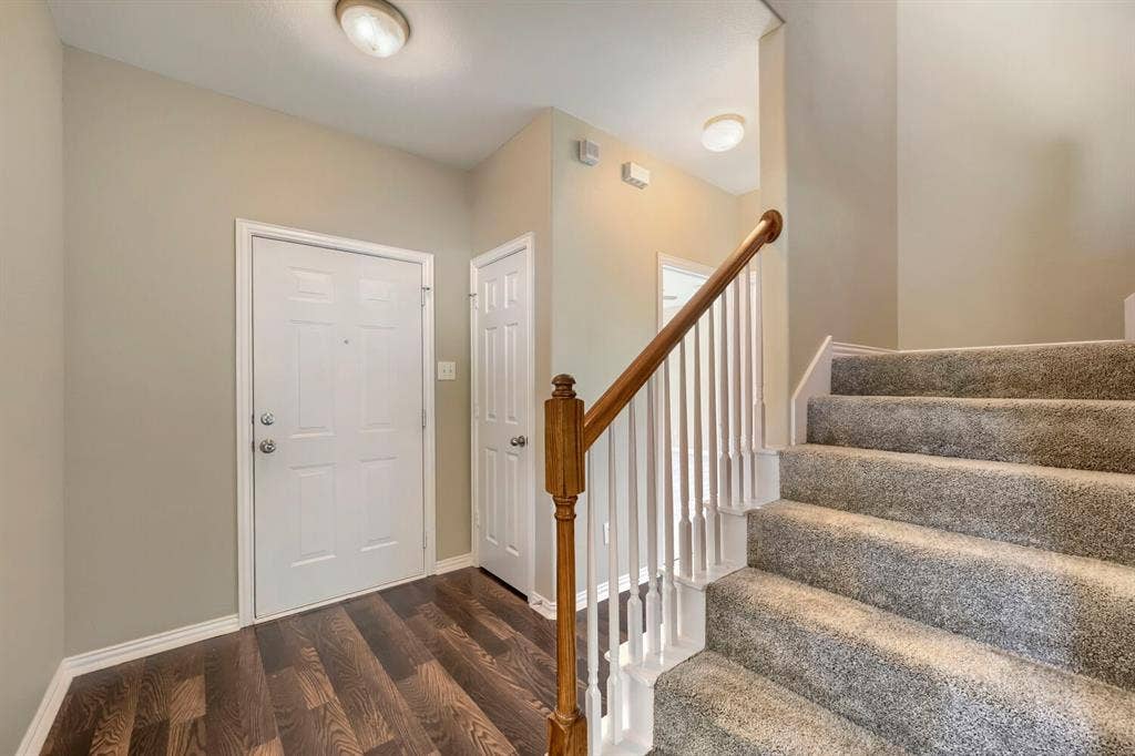Entryway with wood-finish flooring, two panel doors, and a carpeted staircase featuring a wood handrail with white balusters