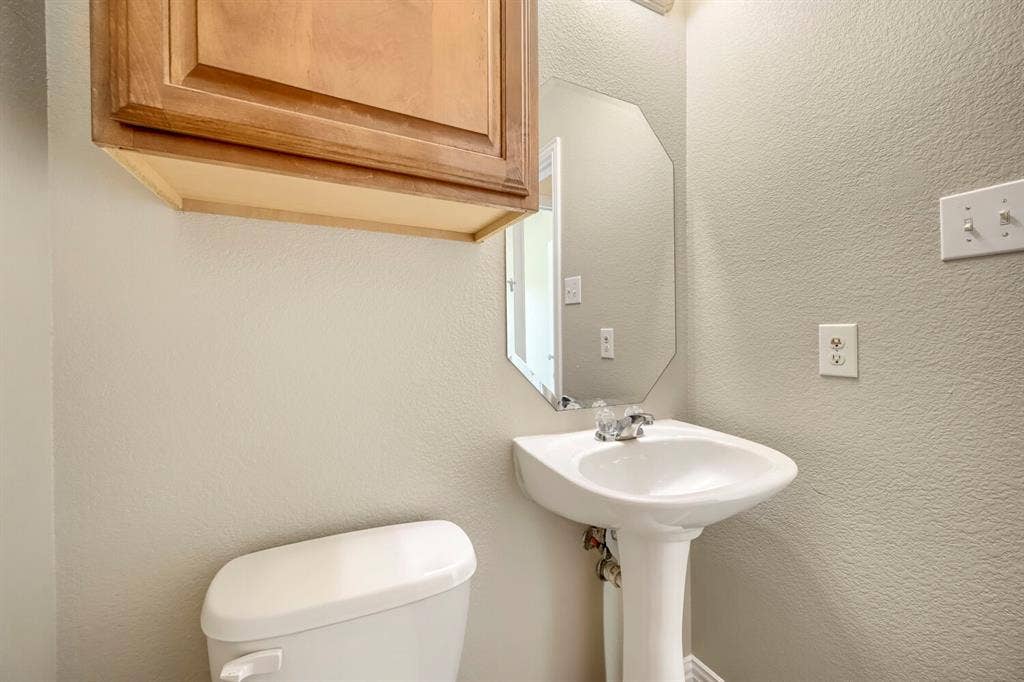 Pedestal sink with chrome faucet, octagonal wall mirror, light wood-finish cabinetry, and neutral wall tones