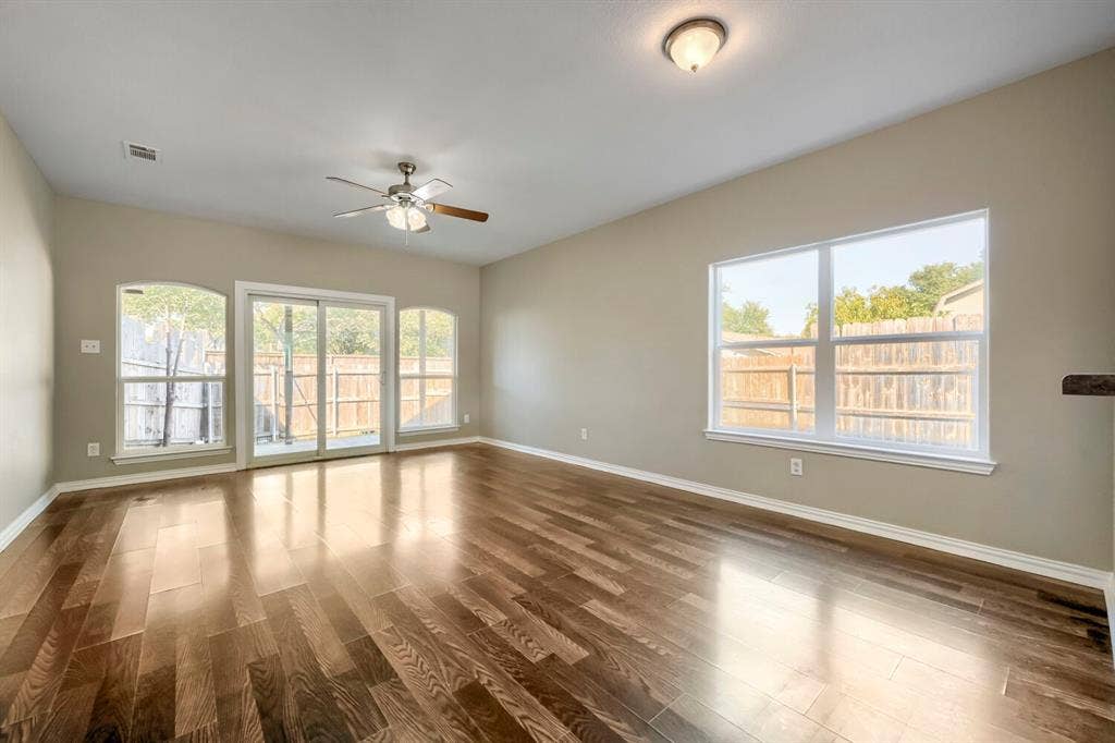 Rich wood-finish flooring, sliding glass patio doors, multiple large windows, and a ceiling fan with integrated lighting