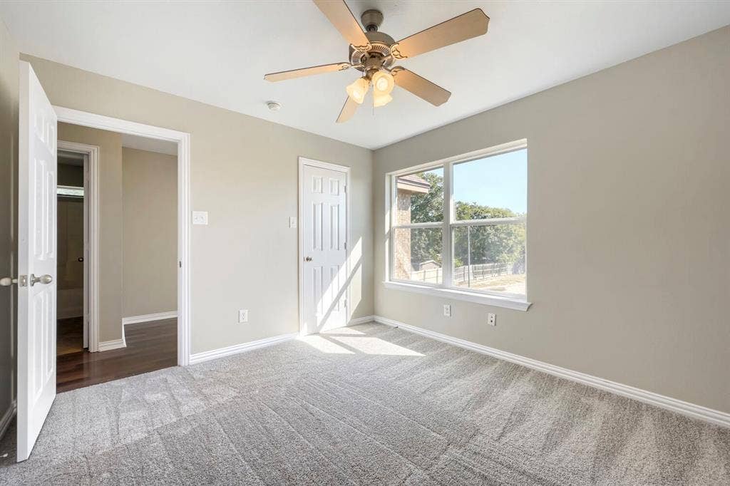 Neutral-toned walls, gray carpeting, and a ceiling fan with integrated lighting