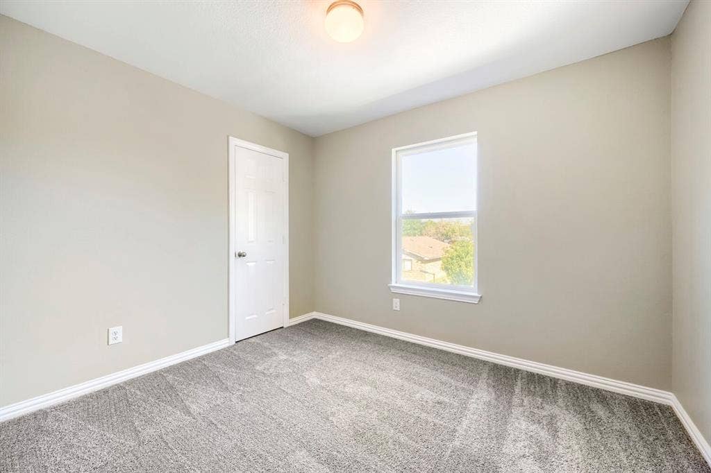 Neutral tone wall paint, textured carpeting, single window with roller shade, white trim, and a ceiling-mounted light fixture