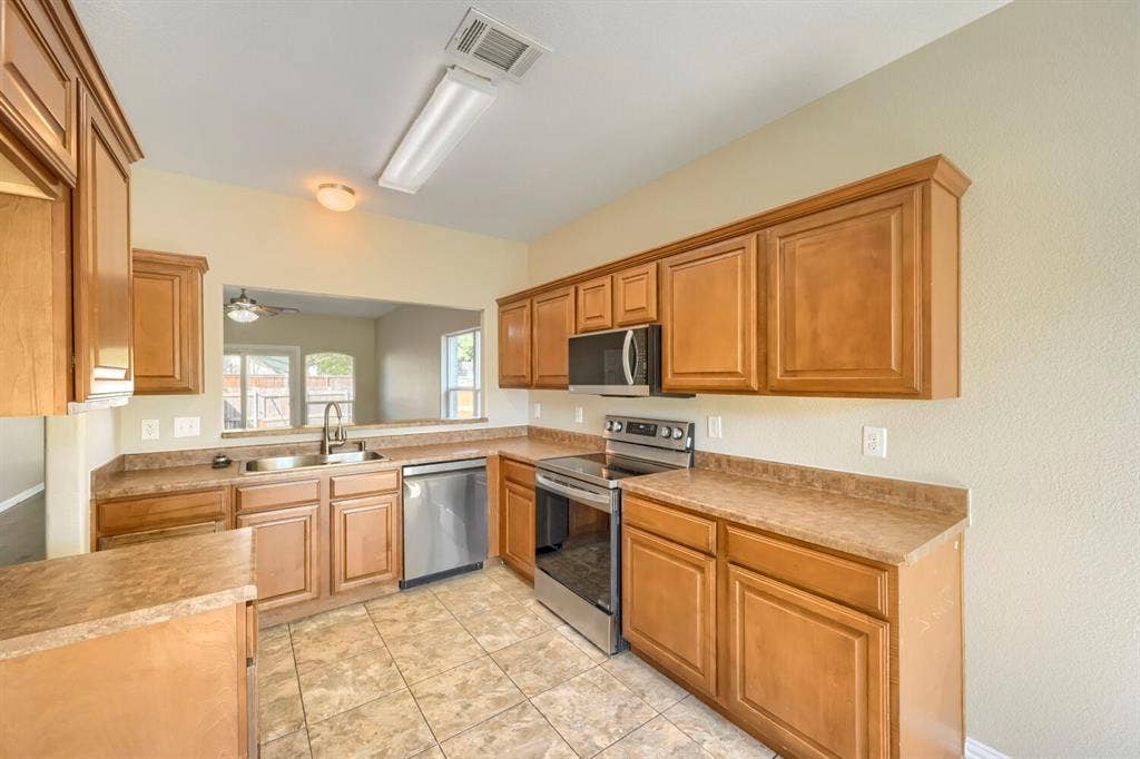 Kitchen featuring wood-finish cabinetry, stainless steel appliances, a dual basin sink, and tile flooring