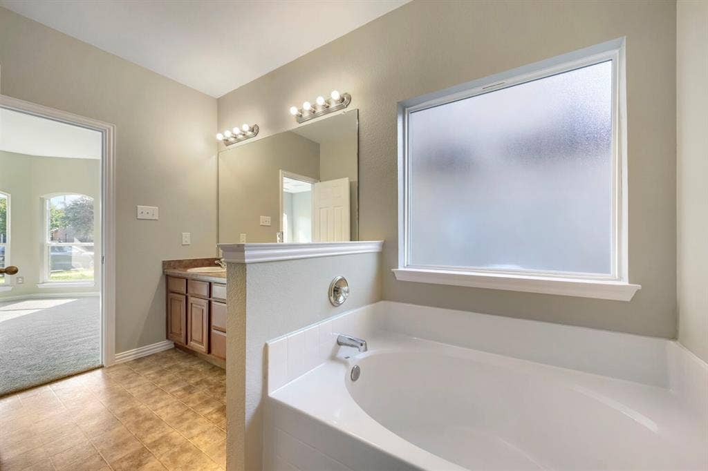 Built-in soaking tub with chrome fixtures, frosted privacy window, and tile flooring