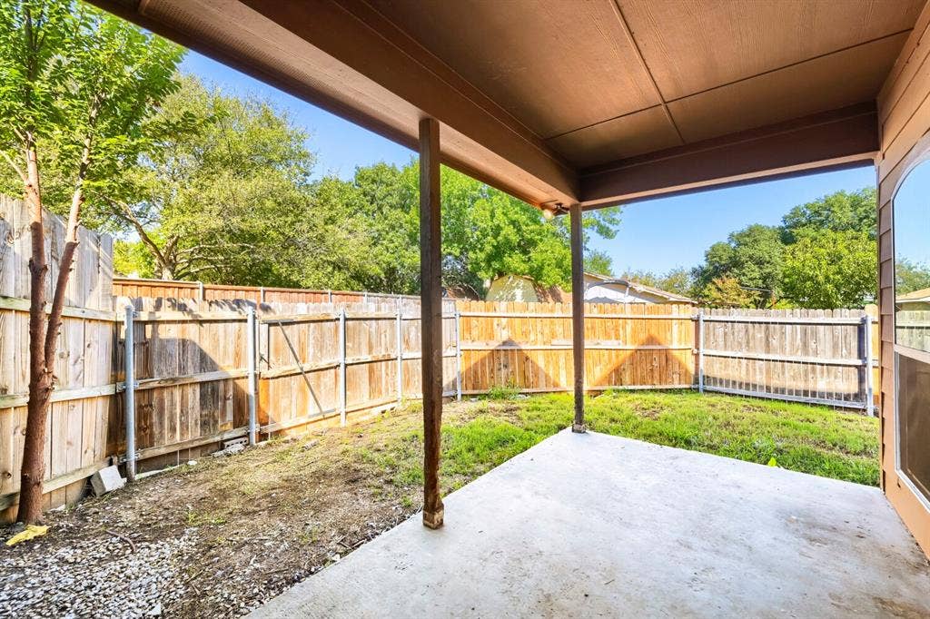 Covered concrete patio with wooden support columns, enclosed by wood fencing and a grassy yard