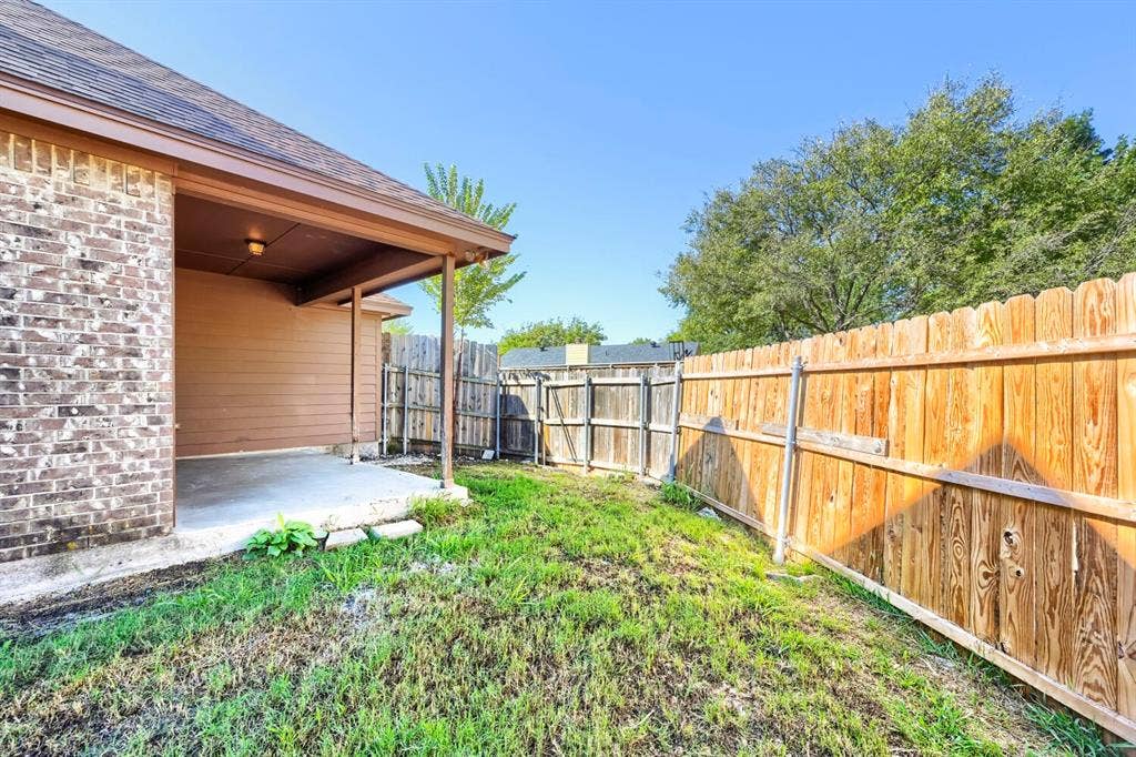 Covered patio with concrete flooring, brick exterior, and wood fencing