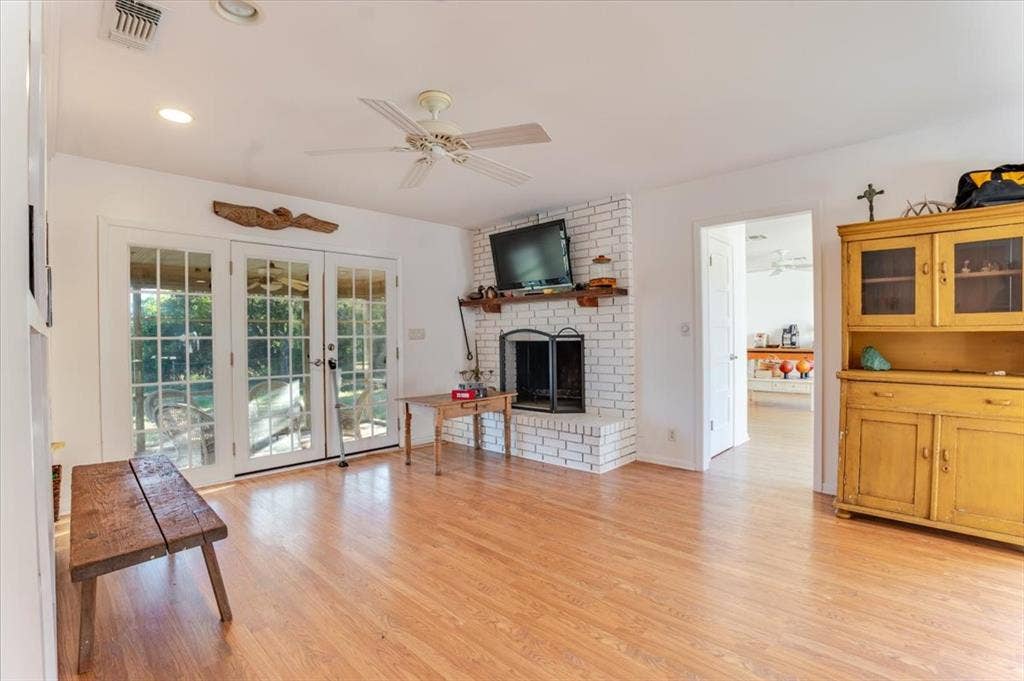 Wood-finish flooring, white brick fireplace, ceiling fan, recessed lighting, and French doors