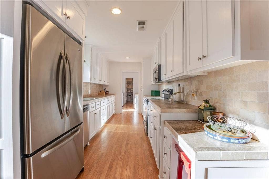 Galley kitchen featuring wood-finish flooring, white cabinetry, light-toned countertops, tile backsplash, and recessed lighting