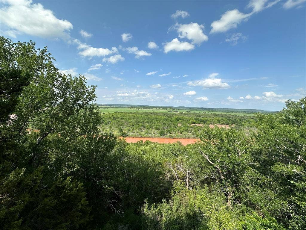 Expansive landscape featuring diverse tree canopy, natural water body, and distant green fields