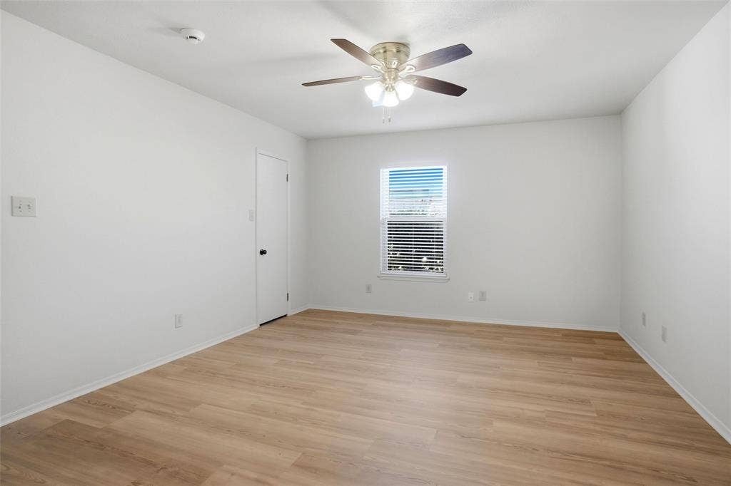 Bright interior with wood-finish flooring, a ceiling fan with integrated lighting, and a single window with blinds