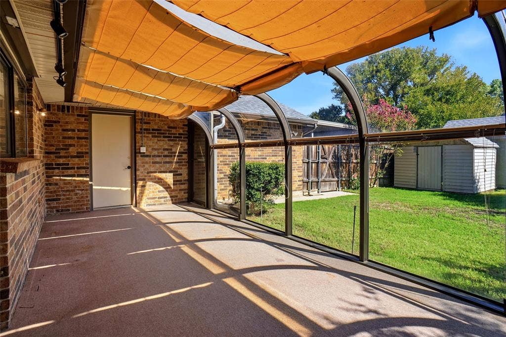 Enclosed sunroom with a curved glass ceiling and retractable shades, brick exterior wall, and direct access to a manicured lawn
