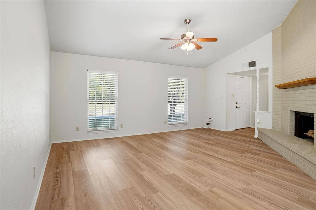 Vaulted ceiling, wood-finish flooring, white brick fireplace with hearth, white window blinds, and ceiling fan
