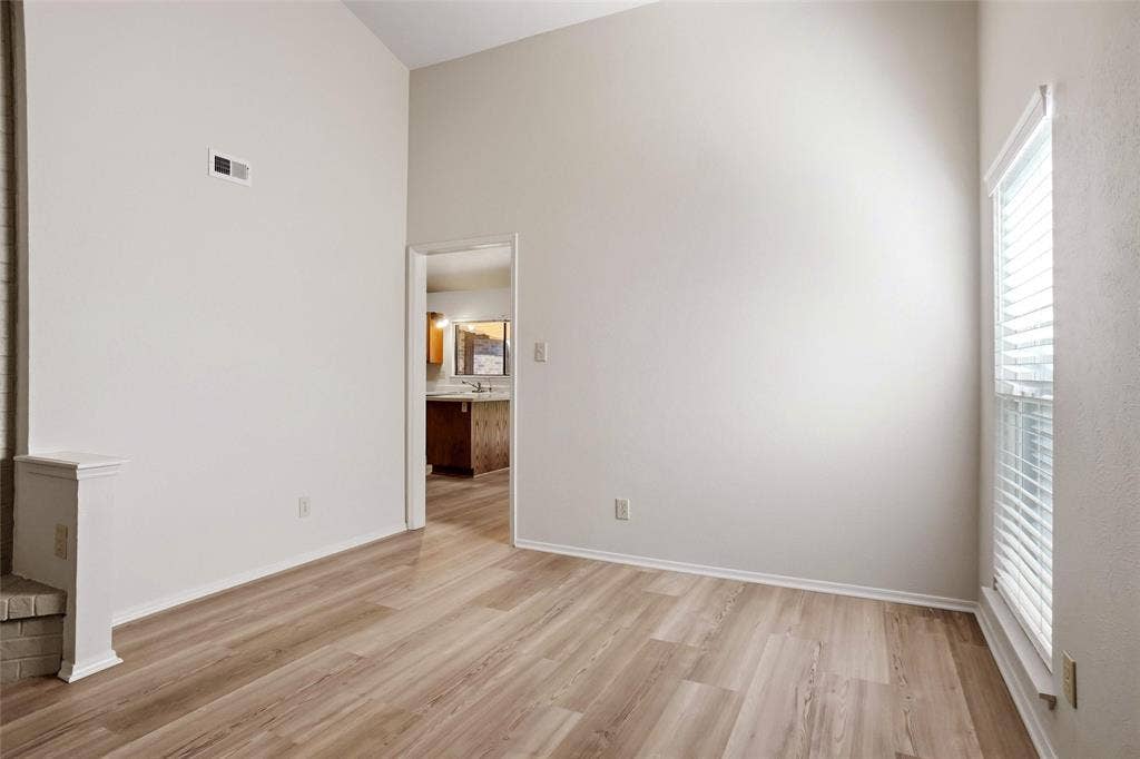 Vaulted ceiling, wood-finish flooring, white walls, window with blinds, and white trim
