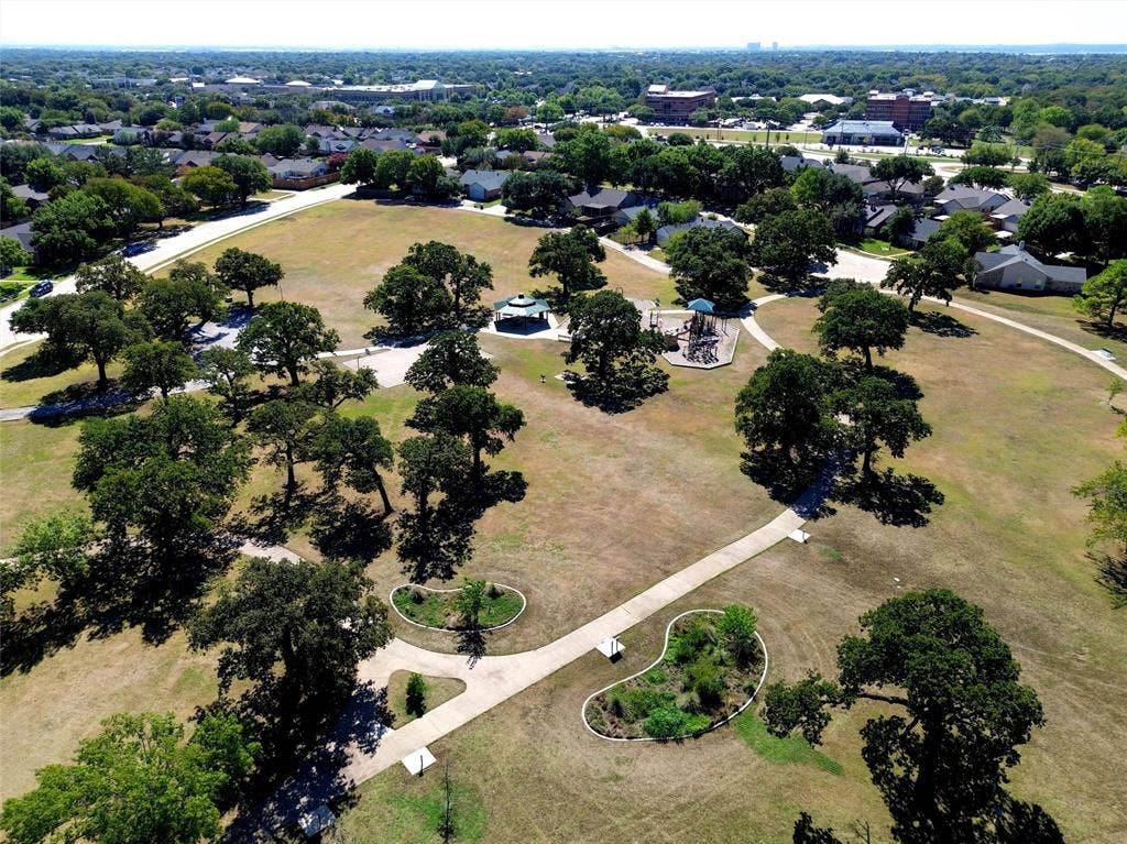 Expansive parkland with mature trees, paved walking paths, a playground structure, and a covered gazebo
