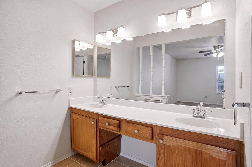 Dual basin vanity with wood-finish cabinetry, white countertop, and prominent wall-mounted mirror