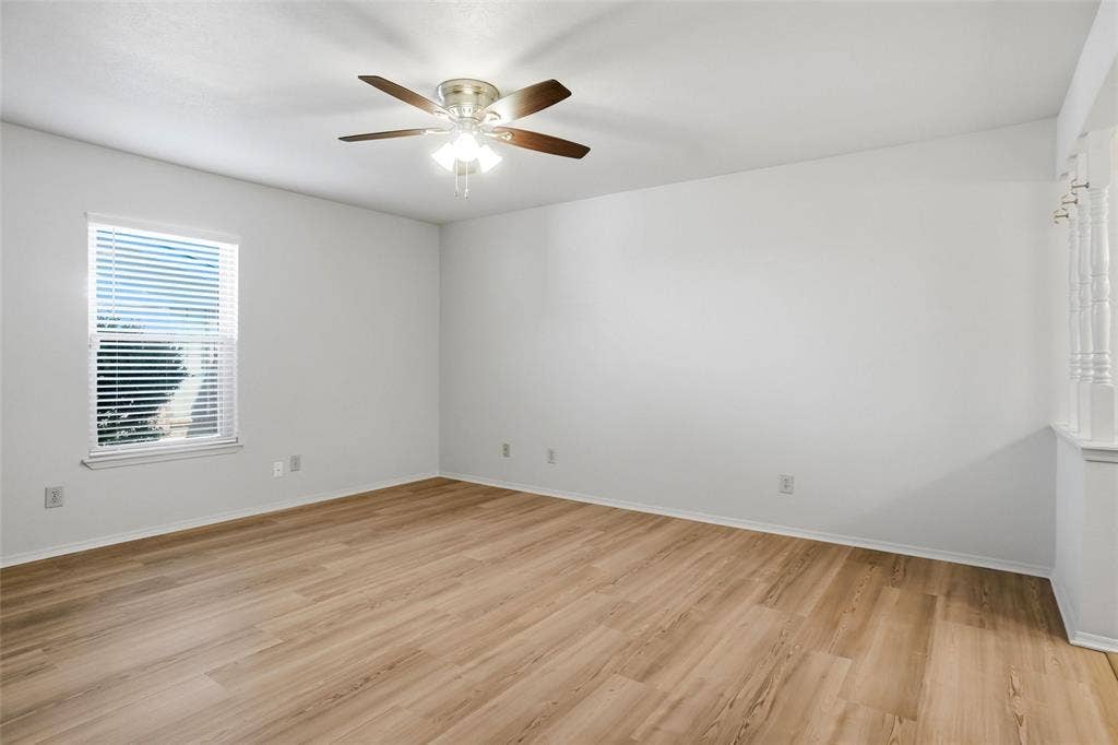 Spacious interior with wood-finish flooring, a ceiling fan with integrated lighting, and a window with blinds