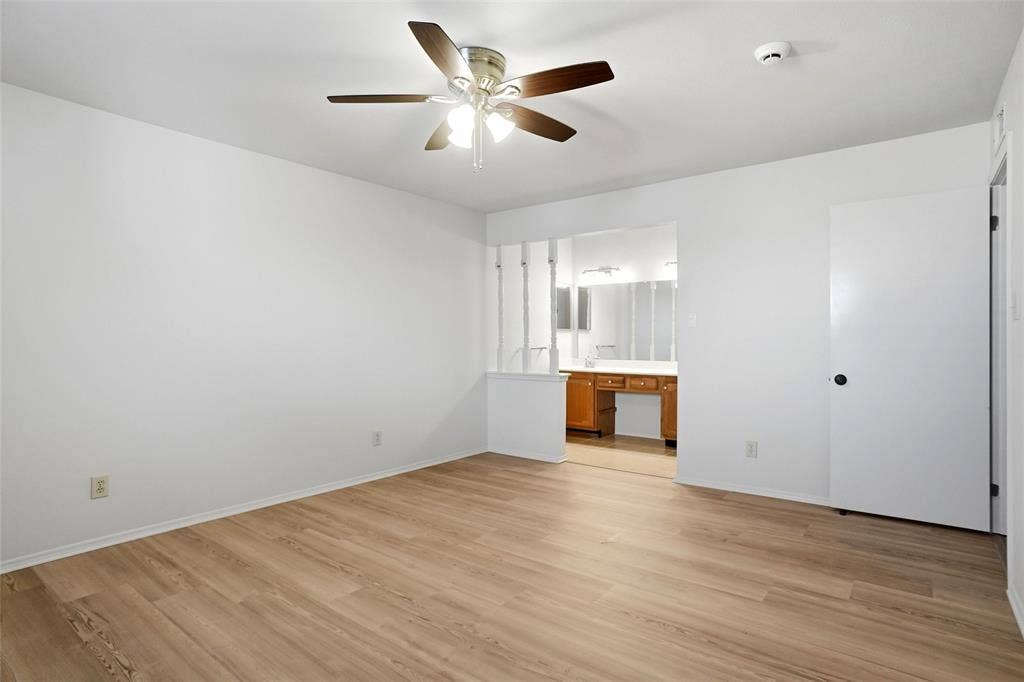 Wood-finish flooring, ceiling fan, white interior walls, white door, and built-in vanity with wood-finish cabinetry