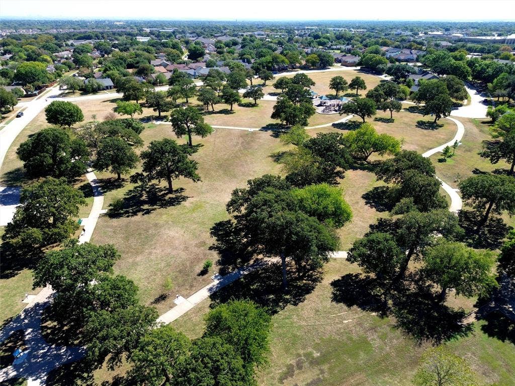 Expansive park area featuring numerous mature trees, winding paved pathways, and verdant green spaces within a residential setting