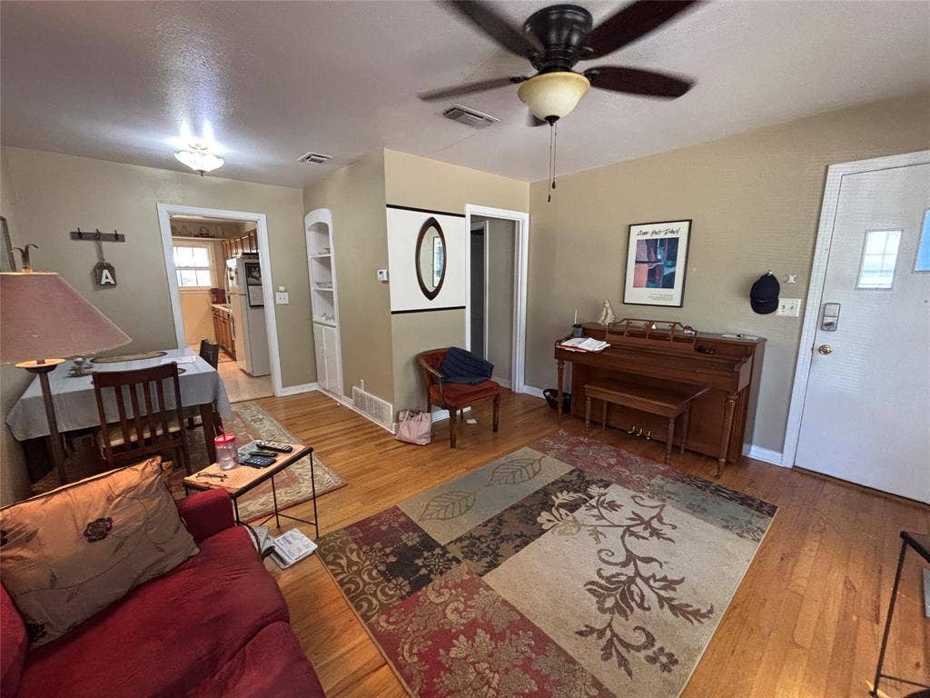 Hardwood flooring, ceiling fan, built-in shelving, kitchen access, and a paneled entry door